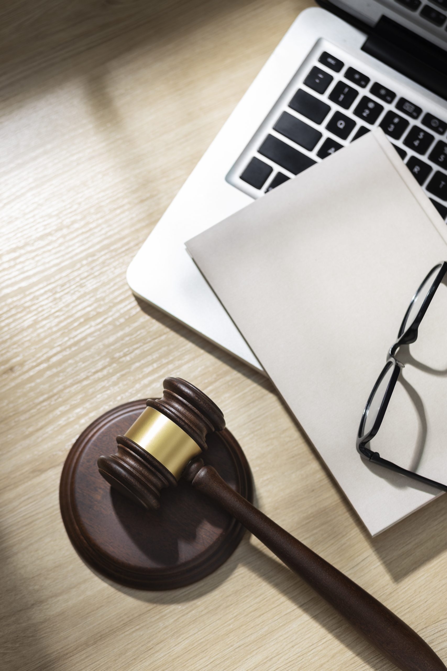 Wooden gavel, laptop, notebook, and eyeglasses on a light wood desk