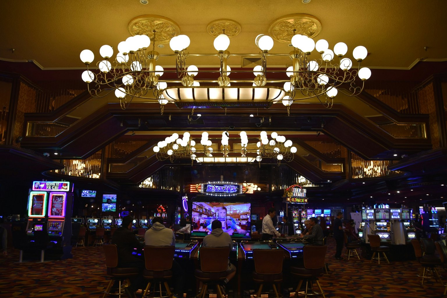 Casino gaming floor with patrons at electronic tables and slot machines under chandeliers, a setting a Las Vegas casino injury lawyer reviews