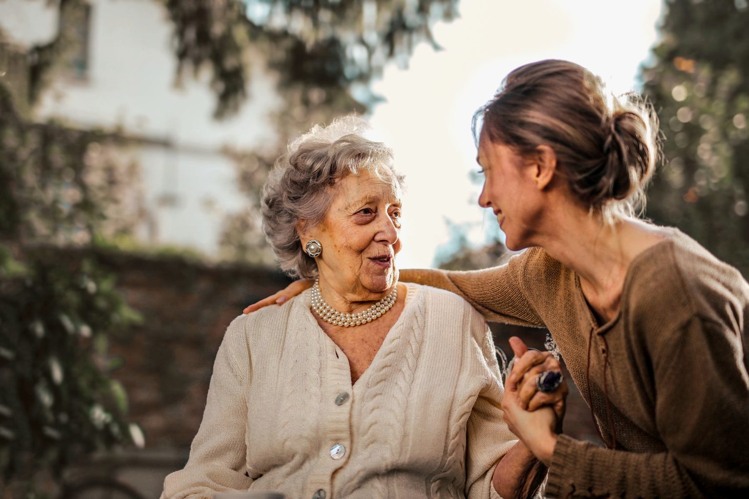 Younger woman holding an older family member's hand in a sunlit garden