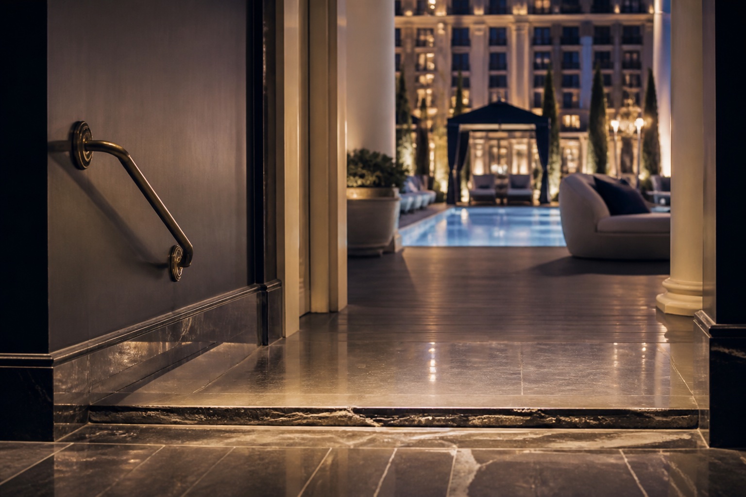 Chipped stone step at a hotel pool threshold at night, with lounge chairs and water beyond