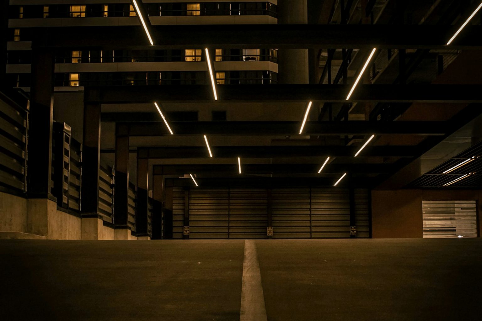 Nighttime parking garage entrance with receding overhead lights and closed rolling doors